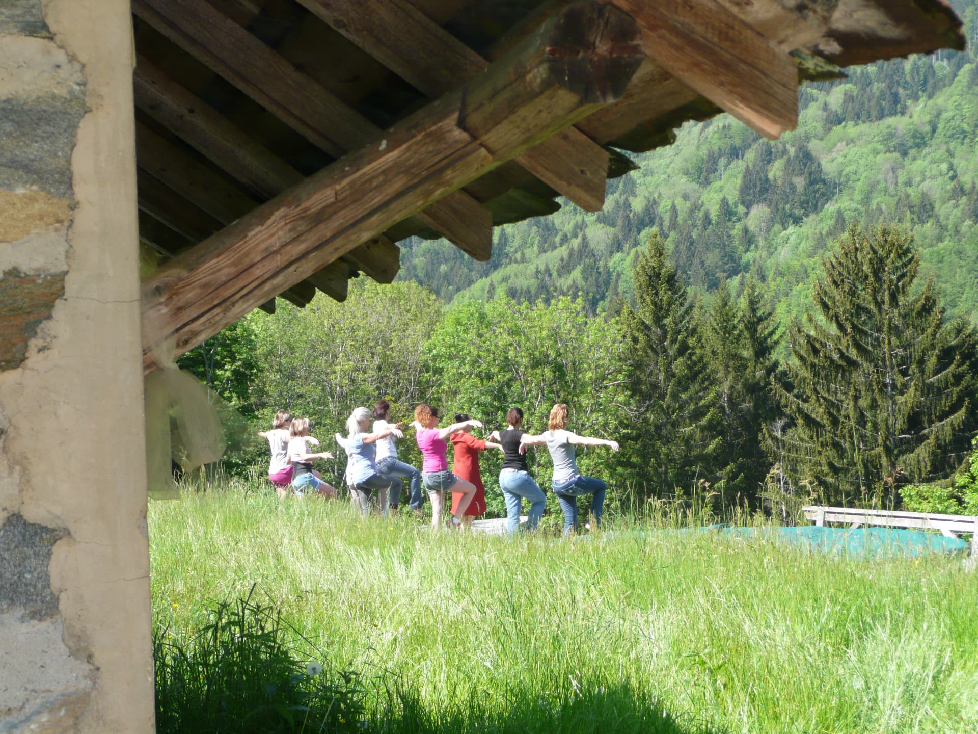 Groupe pratiquant le Qigong en cercle dans l'herbe, sous le toit d'une grange